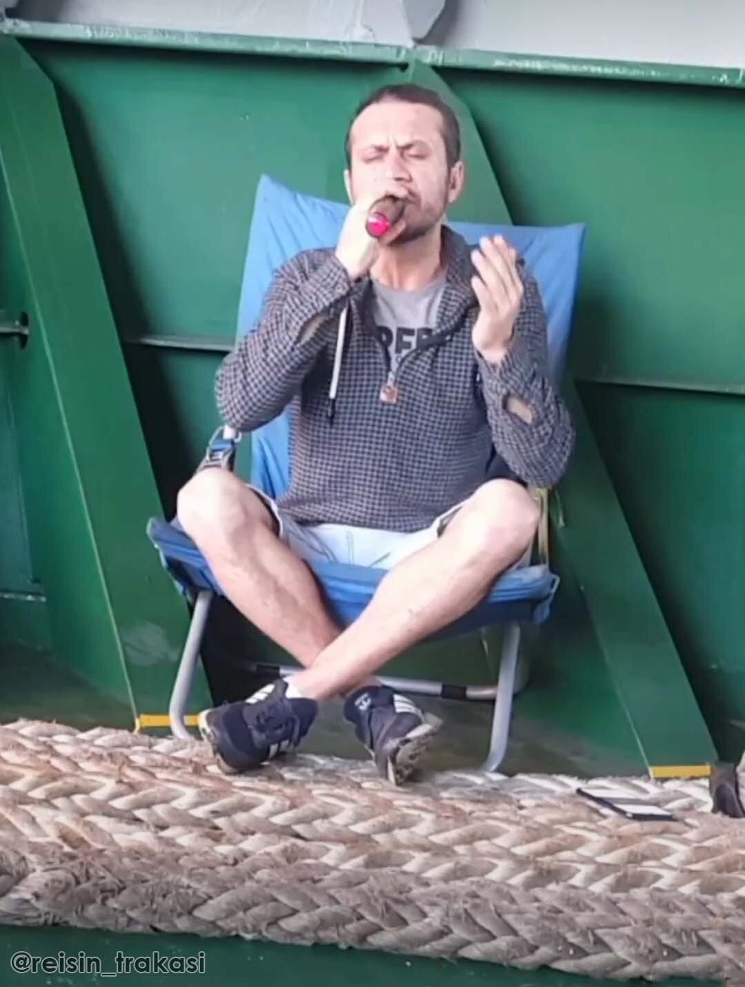 A ship's crew singing while sitting down near the bulkheads with mooring ropes in front of him.