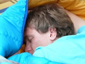 A man on his belly sleeping in bed.