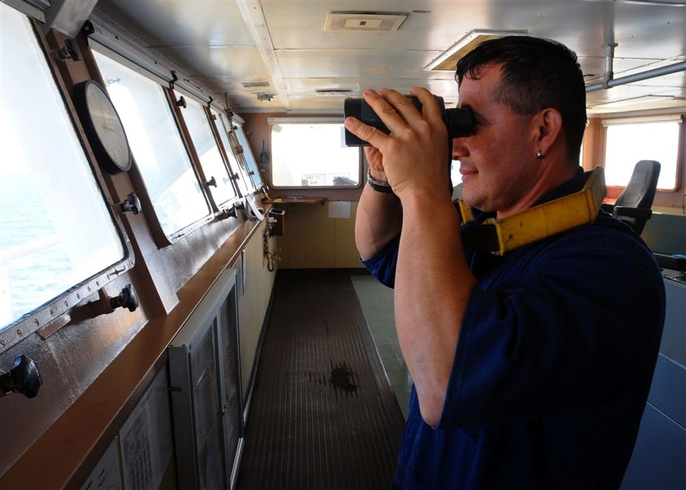 Seaman on the bridge using a binocular  and looking out for target as part of his watch and lookout duties.