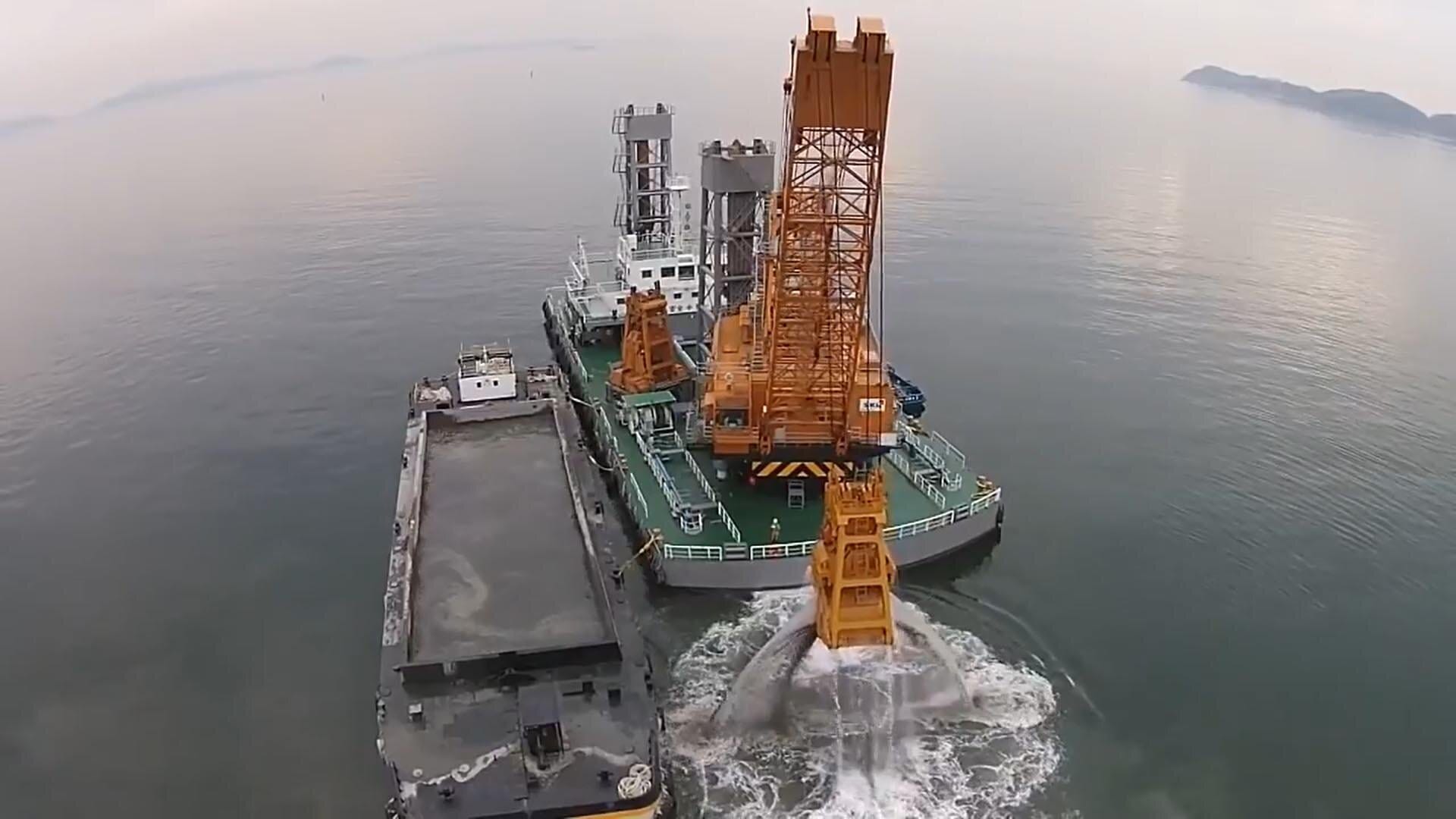 Grab or Clamshell Bucket Dredger transferring the scooped sediments into a small barge beside her.