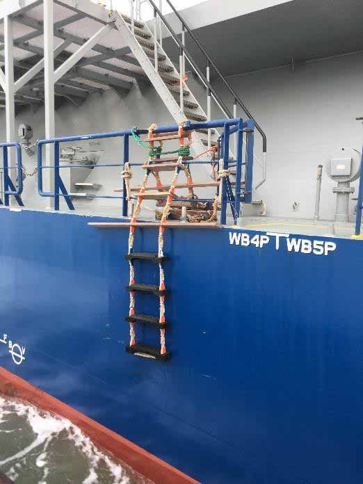 Pilot ladder secured on the ship's railings with the entrance a little further from the ladder itself.