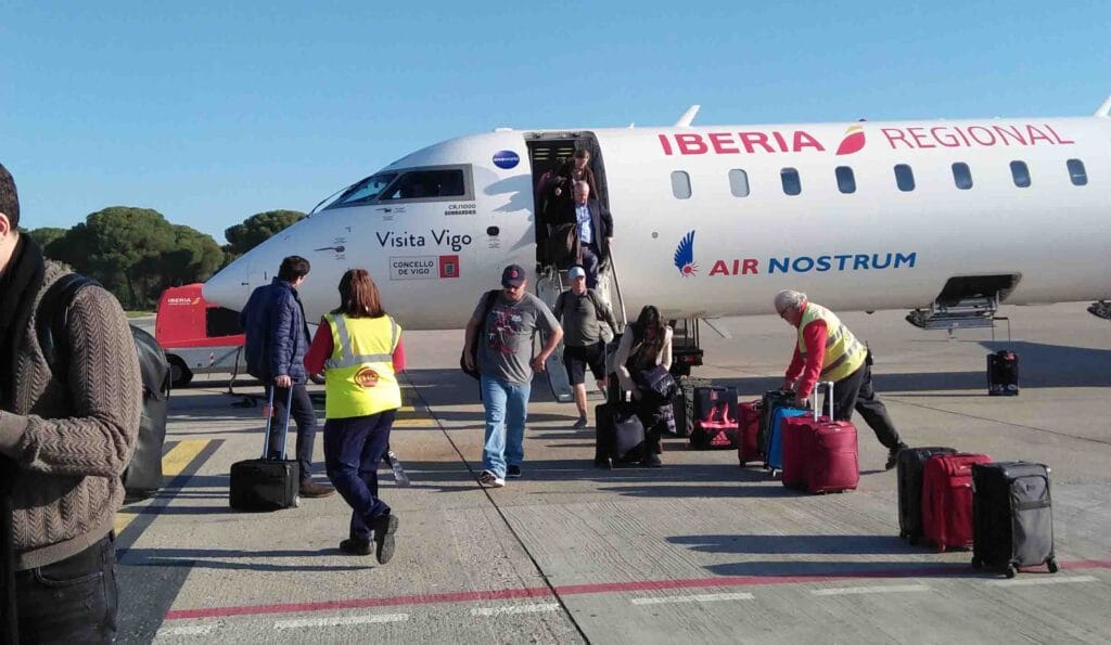 Airline passengers walking towards the airplane while their luggage are brought inside the plane compartment.