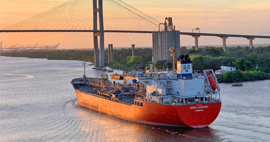A tanker vessel with orange hull approaching a bridge to pass under it.