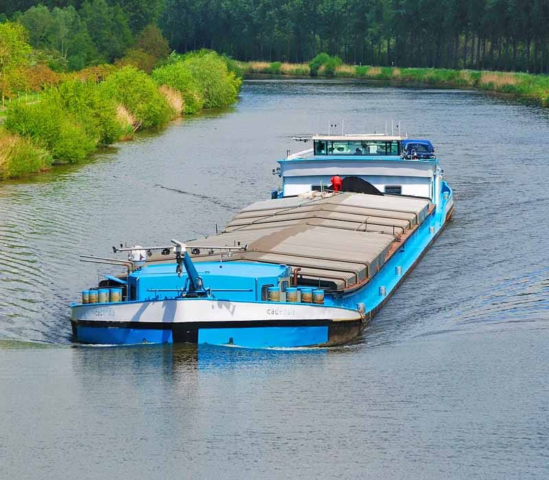 A barge with yellow hull navigating in the middle of the channel.