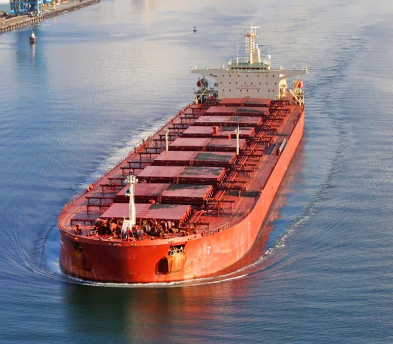A huge orange bulk carrier navigating in the middle of the channel.