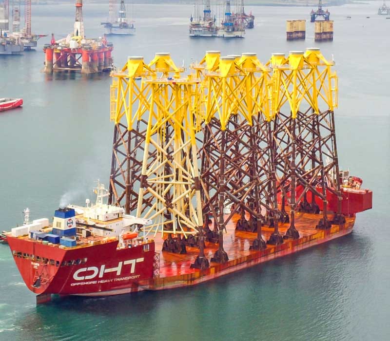 A heavy lift vessel with orange hull carrying jackets for an offshore oil or gas platform.