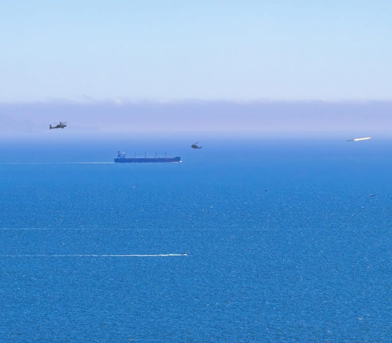 A ship sailing on the blue waters while two helicopters approach it.