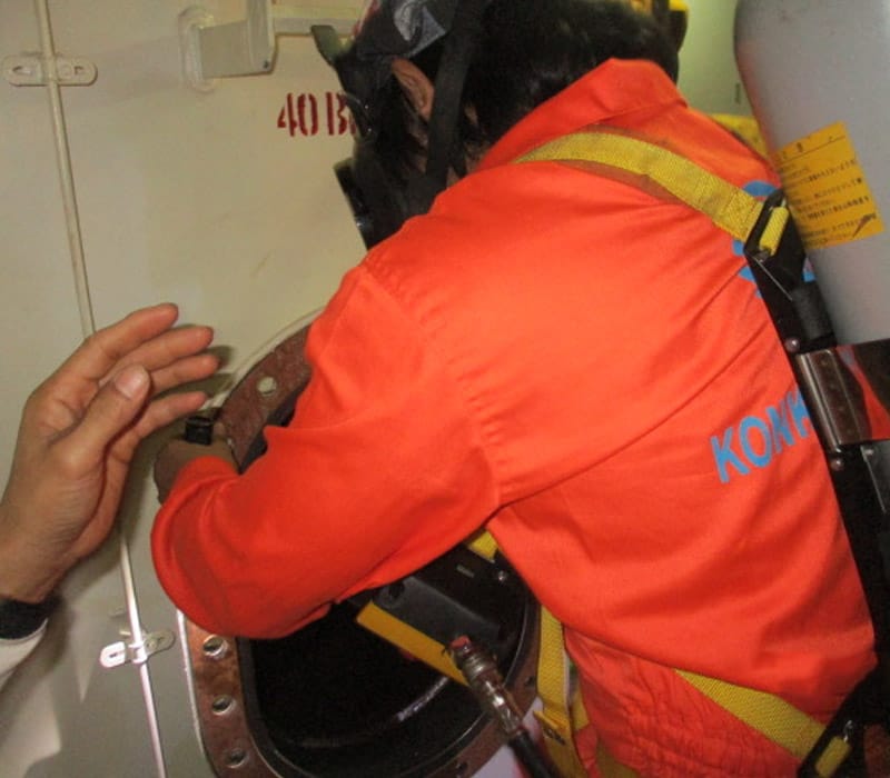A crewmember wearing PPE- SCBA, helmet, coverall, and gas detector entering the MGO Tank.